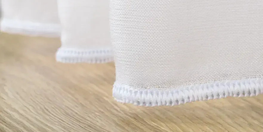Lette tekstiler sys med en dekkende overlocksøm direkte på kanten. Dette gir en ren avslutning og kombineres med sinktyngdebånd for stabilitet og jevnt fall.